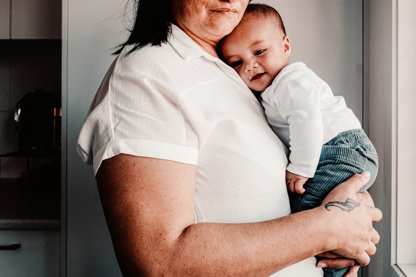 Baby resting against their mum’s shoulder at home